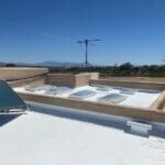 Flat white roof with multiple skylights and a solar panel, showing a well-maintained roofing surface on a clear sunny day.